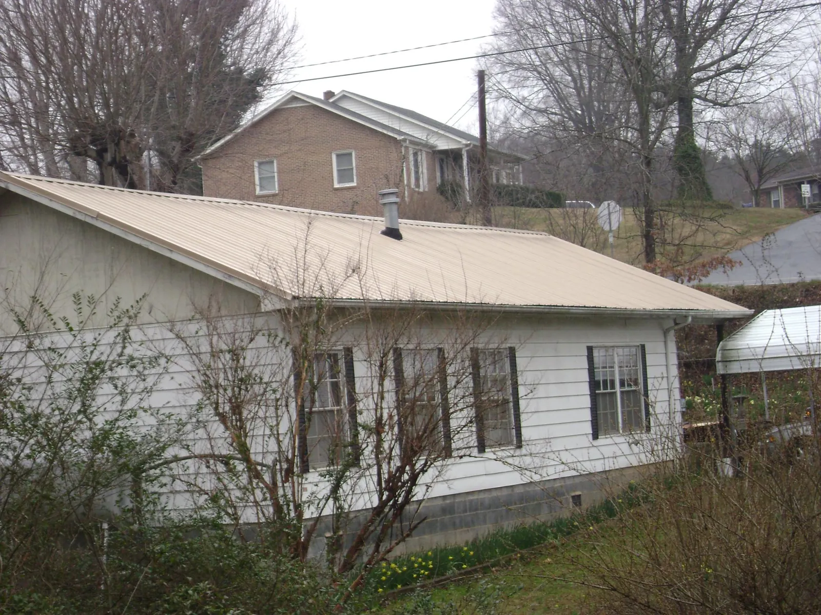 Tan metal roof on a white sided house set into a hillside — Commercial Roofing by Roofing Brothers in Thomaston