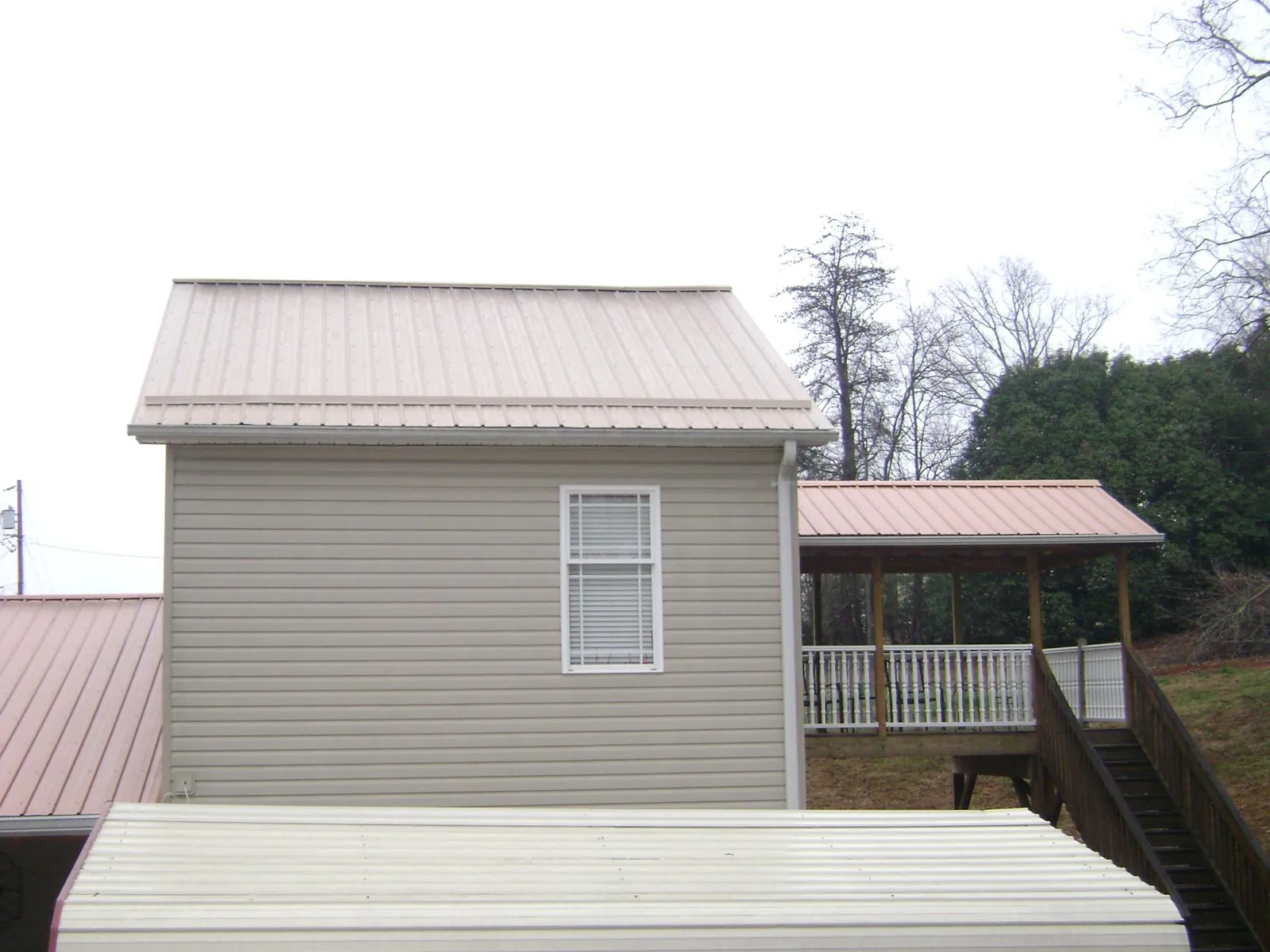 Tan metal roofs on a two story addition and attached porch, from a Roof Replacement job in Thomaston